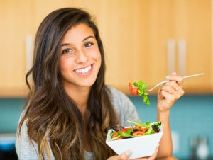 Smuk ung kvinde spiser salat med grøntsager