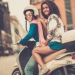 To piger på en cremefarvet scooter